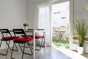 Une pièce avec une table blanche et quatre chaises noires dotées de coussins rouges, une plante en pot et une vue sur un balcon avec une balustrade en bois.