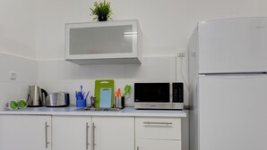 Eine moderne Küche mit weißen Schränken, einer Mikrowelle, einem Wasserkocher und einem Kühlschrank.