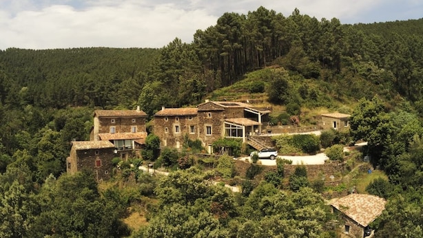A stone building with multiple rooms and a large glass conservatory, surrounded by dense forest. - 12-person house with swimming pool, covered terrace, barbecue, shops nearby (Le Martinet)