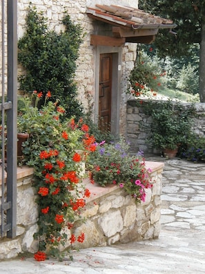 Un edificio de piedra con una puerta de madera, rodeado por un muro de piedra y un camino de piedra.