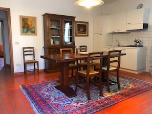 Un comedor con una mesa y sillas de madera, un aparador con puertas de cristal y una cocina con armarios blancos y una estufa.