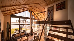 Un vaste espace de vie agrémenté d’une grande fenêtre donnant sur un paysage magnifique, d’un coin salon confortable et d’un escalier en bois.
