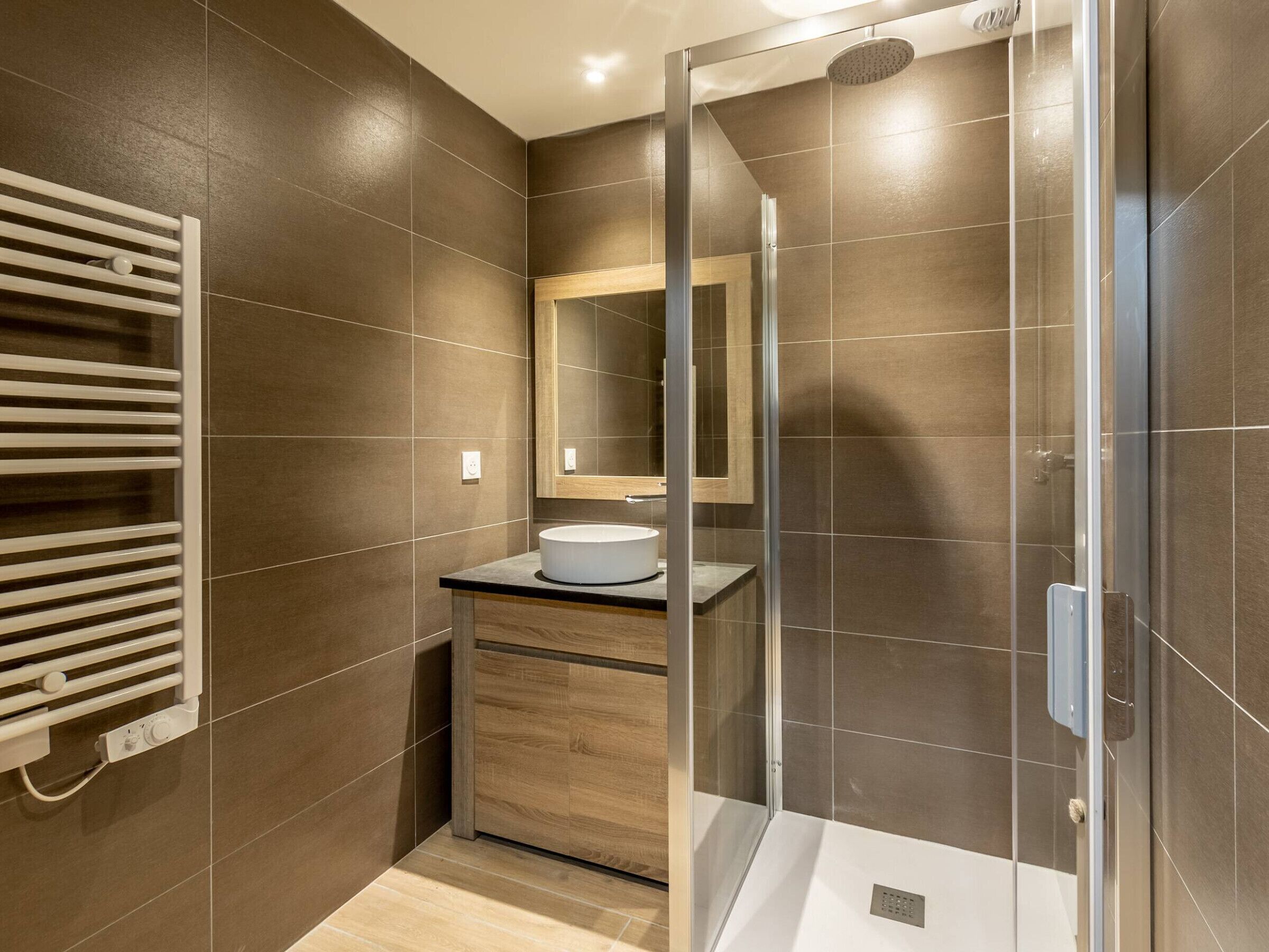 A modern bathroom with a glass-enclosed shower, a wooden vanity with a sink, and a towel rack.