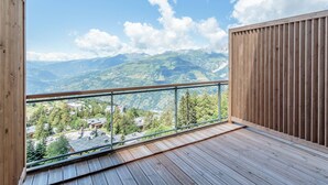 A wooden balcony with a metal railing overlooking a mountainous landscape.