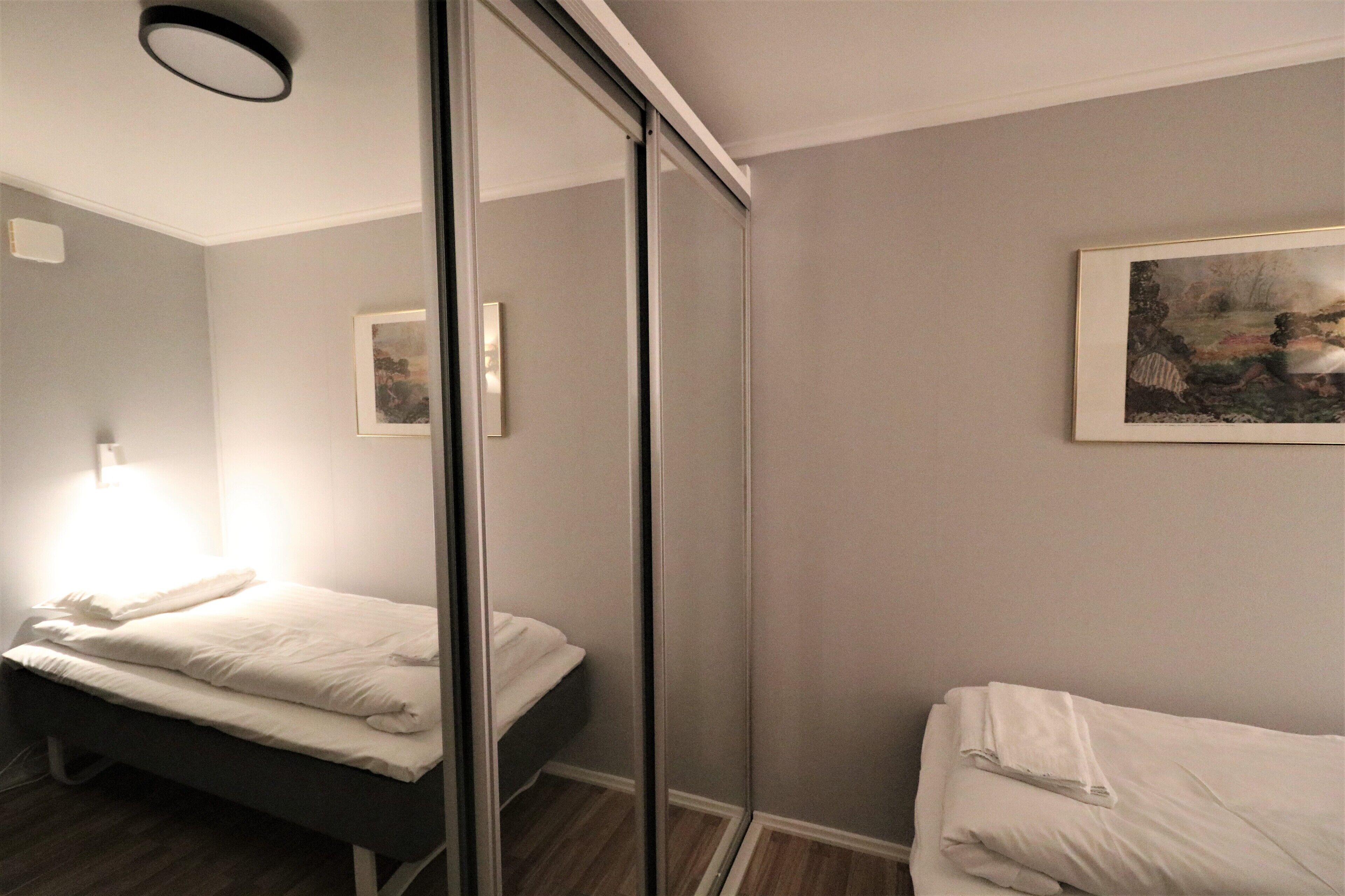 A hotel room with a bed, a bedside table, a mirror, and a painting on the wall.