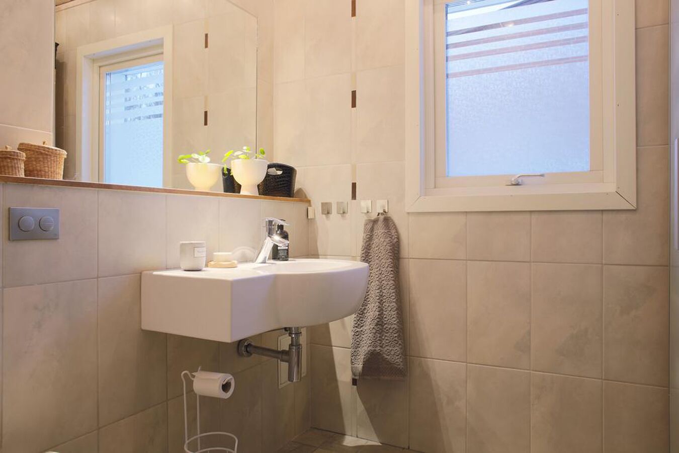 Ein Badezimmer mit einem weißen Waschbecken, einem Spiegel, einem Fenster und einem Handtuch, das an der Wand hängt.