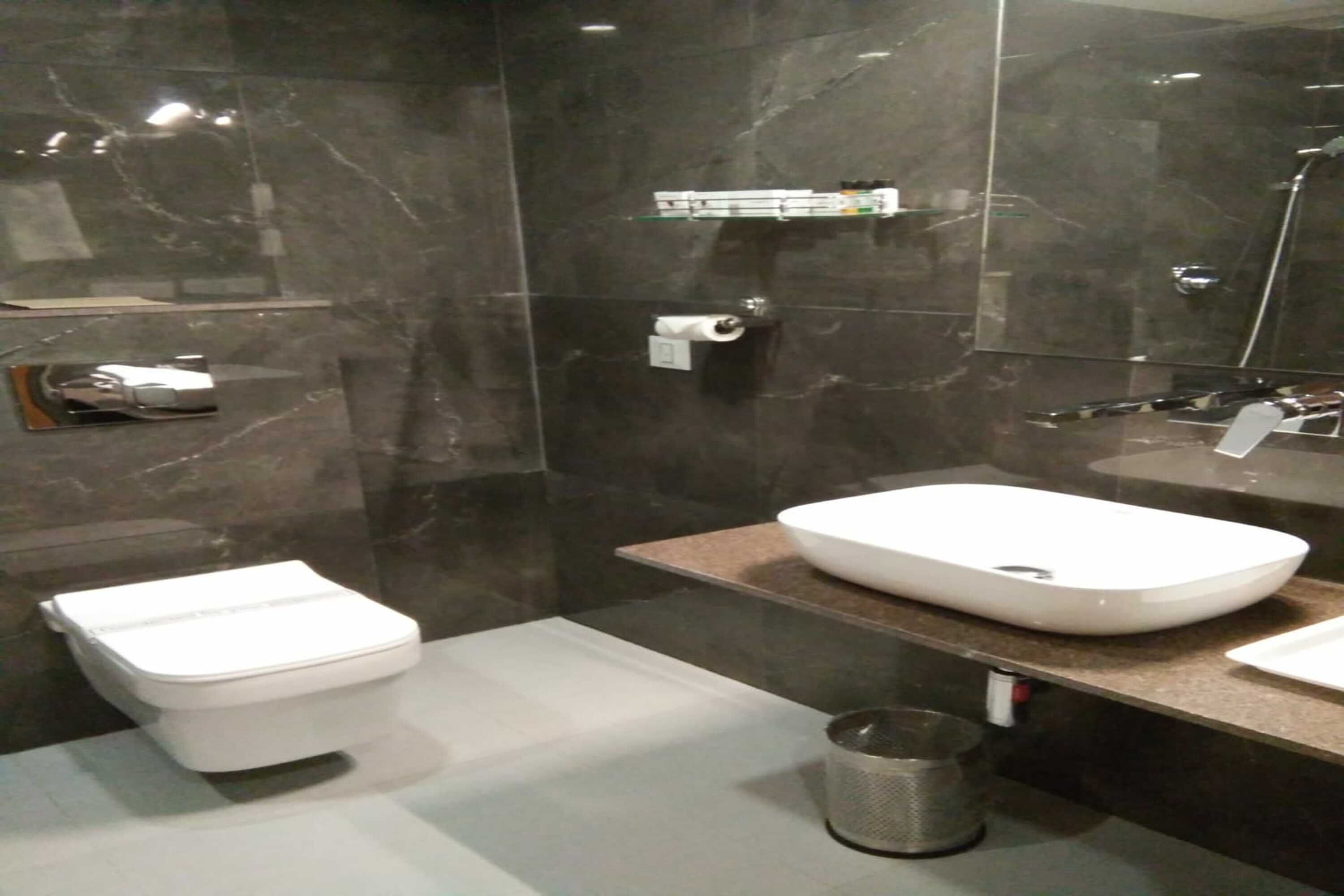 A modern bathroom with a white toilet, a large mirror, a marble backsplash, and a countertop with a sink and a trash can.