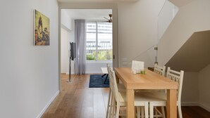 Un coin repas avec une table en bois et des chaises blanches, un tapis bleu et un tableau accroché au mur.