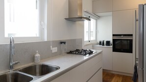 Une cuisine moderne dotée de deux éviers en acier inoxydable, d’une cuisinière à gaz, d’un four encastré et de meubles de rangement blancs.