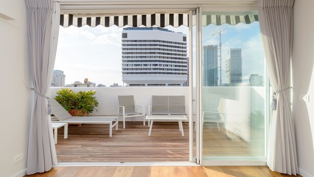 Un balcon doté d’un plancher en bois, de chaises blanches, d’une petite table et d’une plante en pot.
