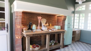 A kitchen with a brick wall, a wooden table with tea and fruit, and a vintage toaster. - Le Manoir des Chevaux Dorés (Le Neubourg)
