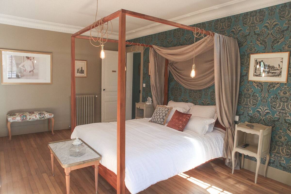 Ein Himmelbett mit Baldachin, ein Nachttisch, eine Bank und ein Beistelltisch.