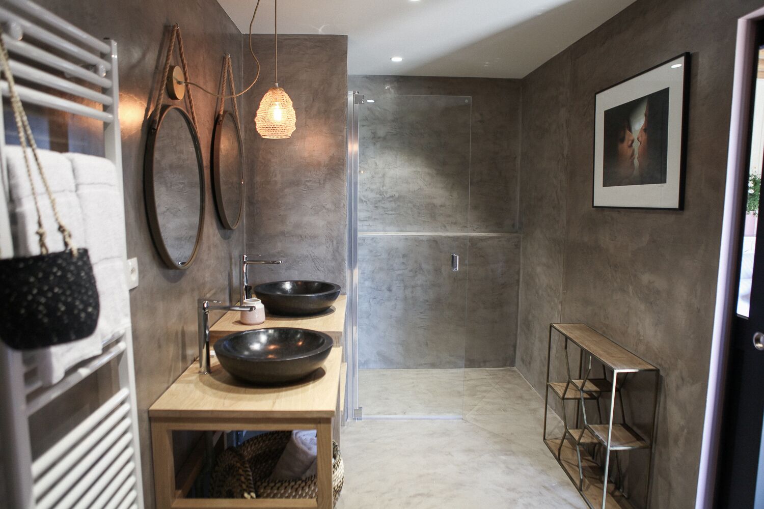 A modern bathroom with two large black bowls on a wooden vanity, a glass shower enclosure, and a framed picture on the wall.