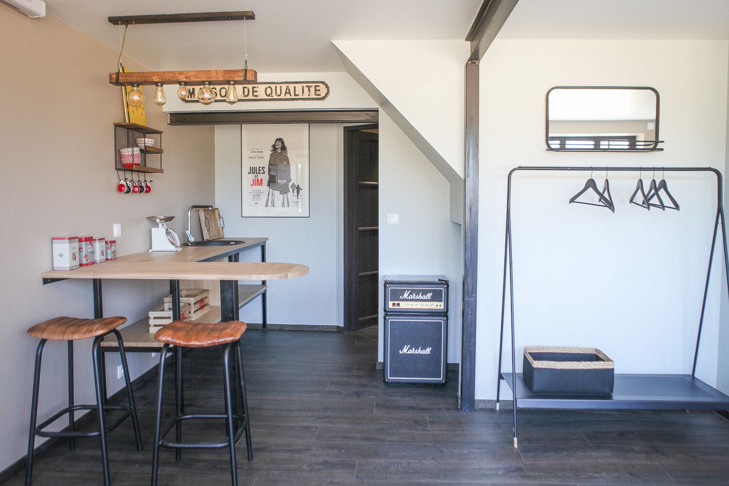 Une cuisine moderne avec une table en bois, des tabourets de bar, un luminaire suspendu, une affiche et un amplificateur Marshall.