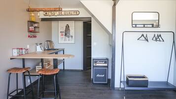 Une cuisine moderne avec une table en bois, des tabourets de bar, un luminaire suspendu, une affiche et un amplificateur Marshall.