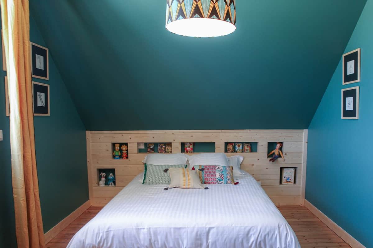 Ein Schlafzimmer mit schrägem Dach, einem Holzkopfende und einem Bett mit weißer Bettwäsche.