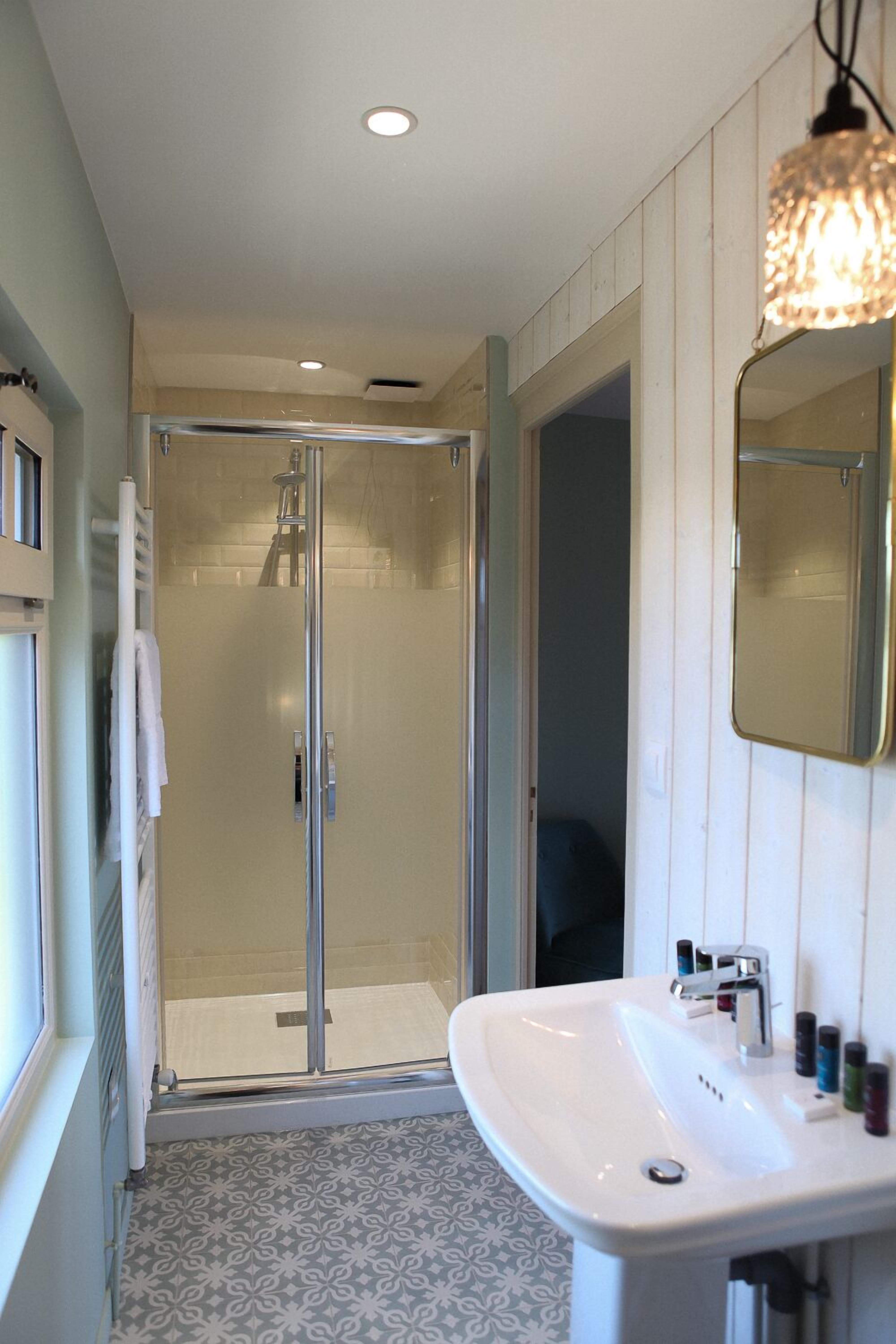 Un bagno con box doccia in vetro, lavabo bianco con specchio e pavimento piastrellato con motivo decorativo.
