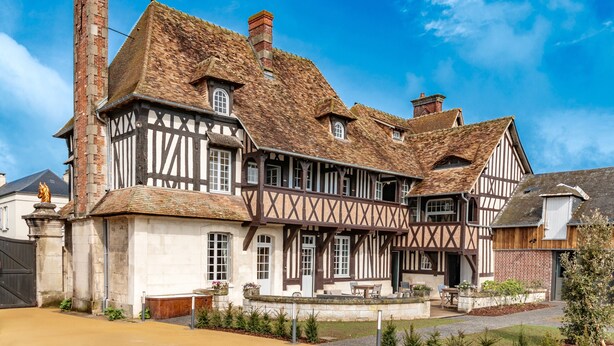 A Tudor-style house with a prominent chimney, multiple windows, and a well-maintained garden. - Le Manoir des Chevaux Dorés (Le Neubourg)