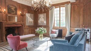 A traditional room with a fireplace, a chandelier, and a sofa set. - Le Manoir des Chevaux Dorés (Le Neubourg)