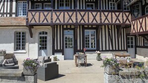 A traditional half-timbered building with a courtyard featuring outdoor seating and flower arrangements. - Le Manoir des Chevaux Dorés (Le Neubourg)