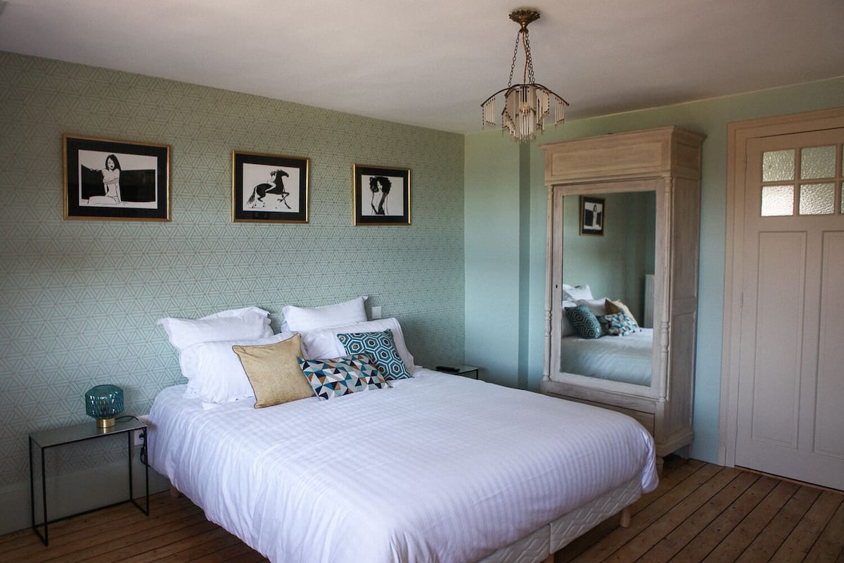 Ein Schlafzimmer mit einem großen Bett, einem Nachttisch, einem Spiegel und drei gerahmten Bildern an der Wand.