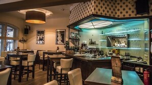 Un espace bar avec des tables et des chaises en bois, un comptoir avec de la verrerie et un mur orné de motifs.