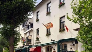 Une vue de l’extérieur d’un hôtel, avec des tables et des chaises à l’extérieur, des plantes en pot et une enseigne indiquant qu’il s’agit de l’hôtel Limburgia.