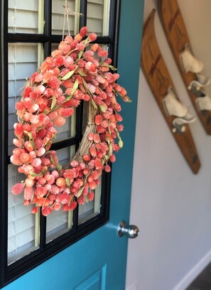 A wreath hanging on a window with a teal door and a wooden wall decoration.