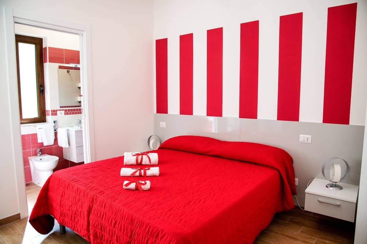 Ein Hotelzimmer mit roter Bettdecke, einem weißen Nachttisch mit Spiegel und einer roten und weißen Streifenwanddekoration.