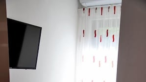 Ein gemütlicher Raum mit einem weißen Schreibtisch, einem Stuhl und einem an der Wand befestigten Fernseher.