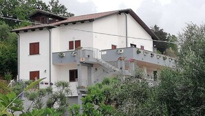 Ein mehrstöckiges Gebäude mit Balkonen, einer Treppe und umgebender Bepflanzung.