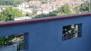 Ein Esstisch ist gedeckt mit Tellern, Tassen und Besteck, mit Blick auf eine Stadtlandschaft mit Gebäuden und Grünflächen.