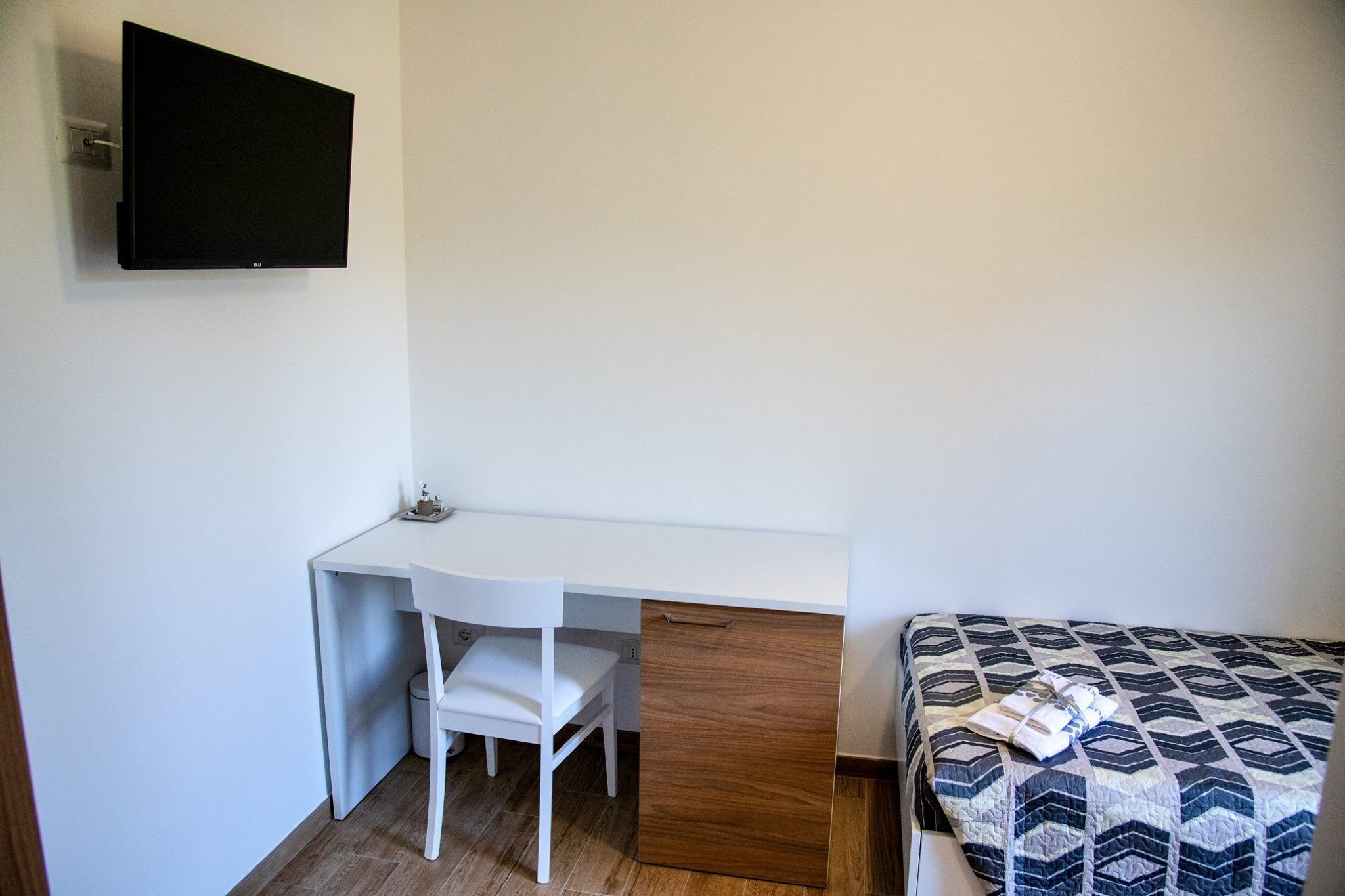 A bedroom with a bed, a desk, a chair, and a TV mounted on the wall.