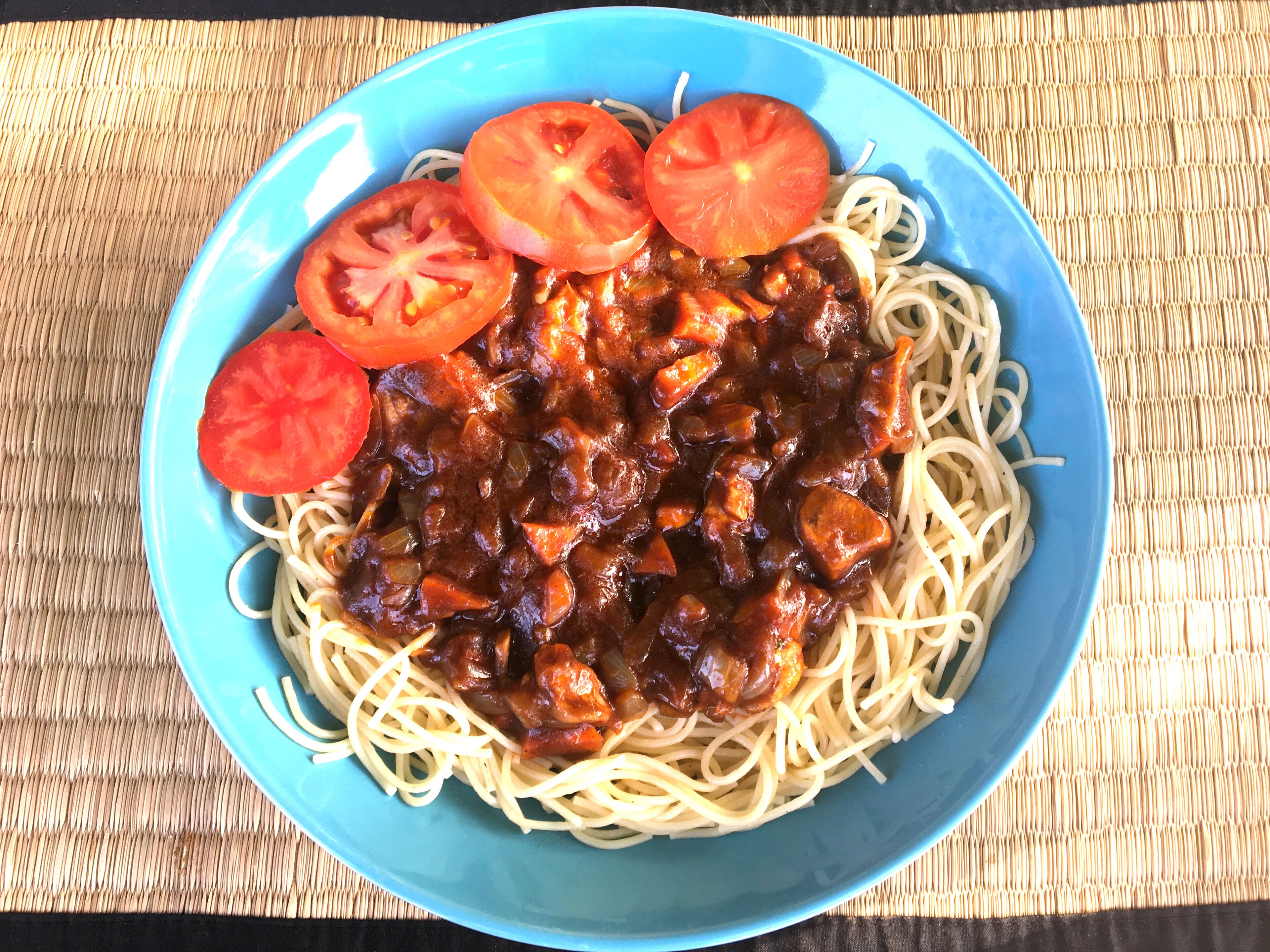 A bowl of spaghetti with a tomato-based sauce and slices of tomato on top.