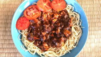 A bowl of spaghetti with a tomato-based sauce and slices of tomato on top.