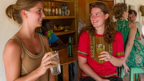 Dos personas sentadas en un bar con estantes llenos de botellas al fondo.