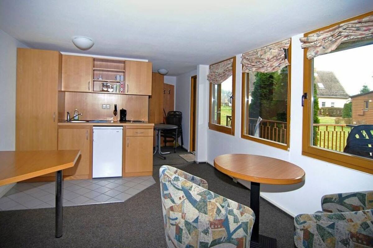 A compact kitchen with wooden cabinets, a white dishwasher, and a dining area with a round table and patterned chairs.