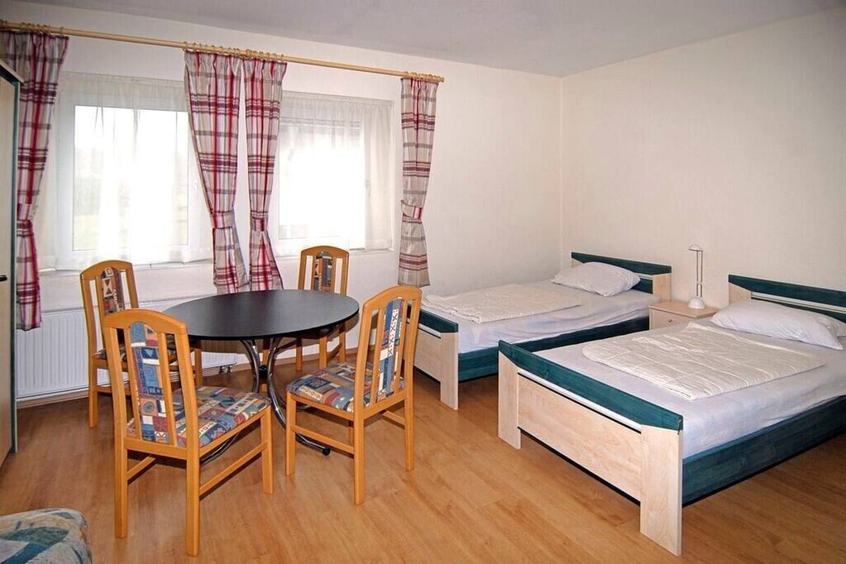 A room with two single beds, a round table with chairs, and a window with curtains.