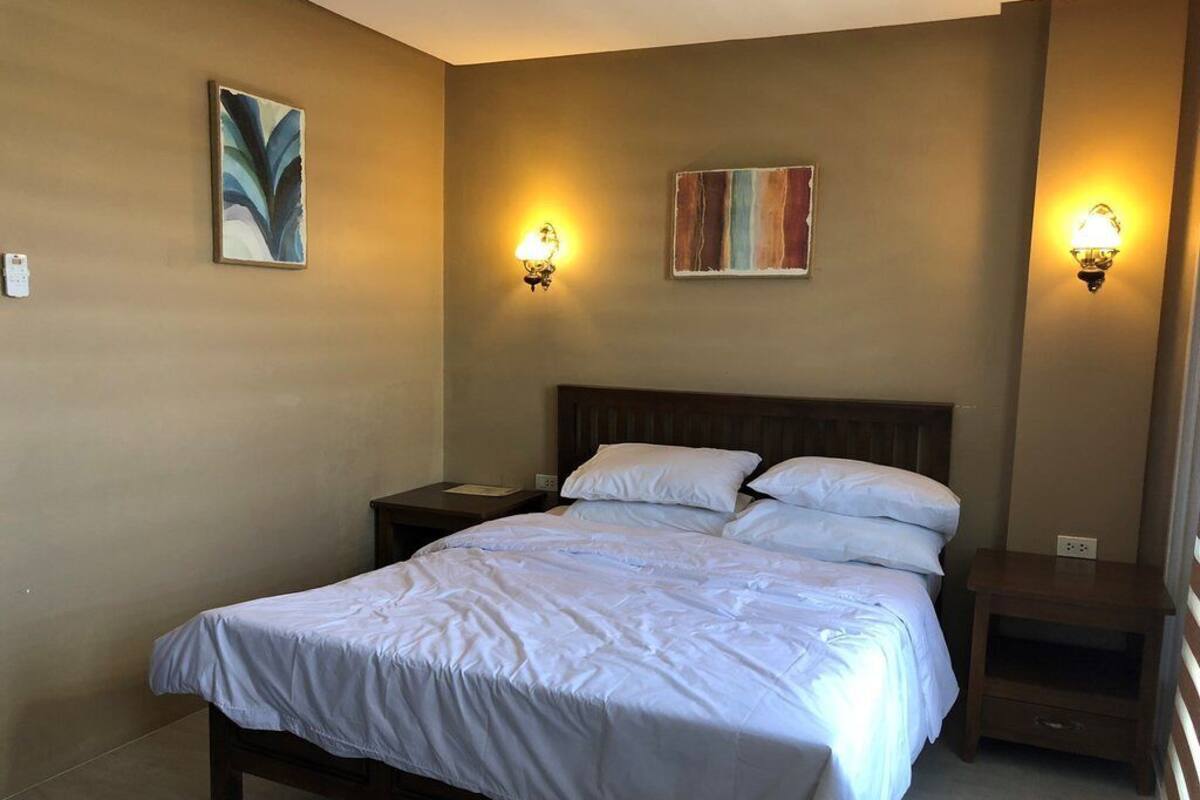 A bedroom with a large bed, two bedside tables, and wall-mounted lamps.