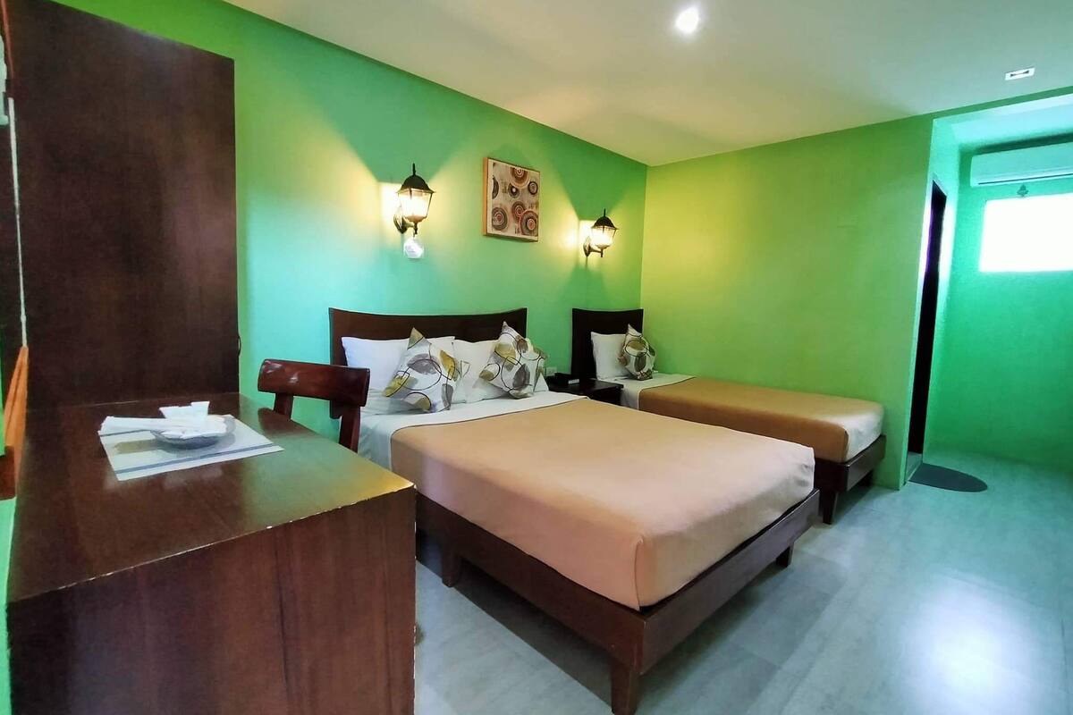 A hotel room with two beds, a wooden desk, and green walls.