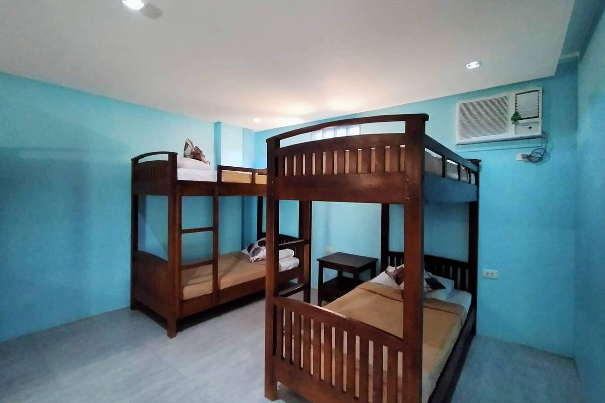 A room with two bunk beds, a small table, and a wall-mounted air conditioner.