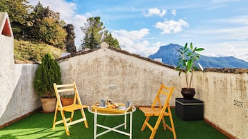 Een terras op het dak, met een tafel, twee stoelen, een plant in pot en uitzicht op bergen.