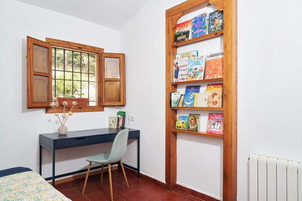 A study room with a desk, chair, bookshelf, and a window with wooden shutters.