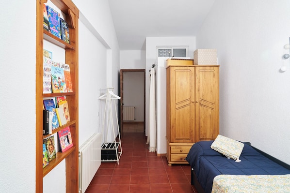 A narrow room with a bookshelf, a wardrobe, a radiator, and a bed.