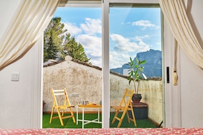 A room with a sliding glass door leading to an outdoor area with two wooden chairs, a small table, and a potted plant.