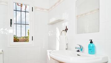Une salle de bain avec un lavabo blanc, un miroir, une fenêtre donnant sur un espace verdoyant et des toilettes.