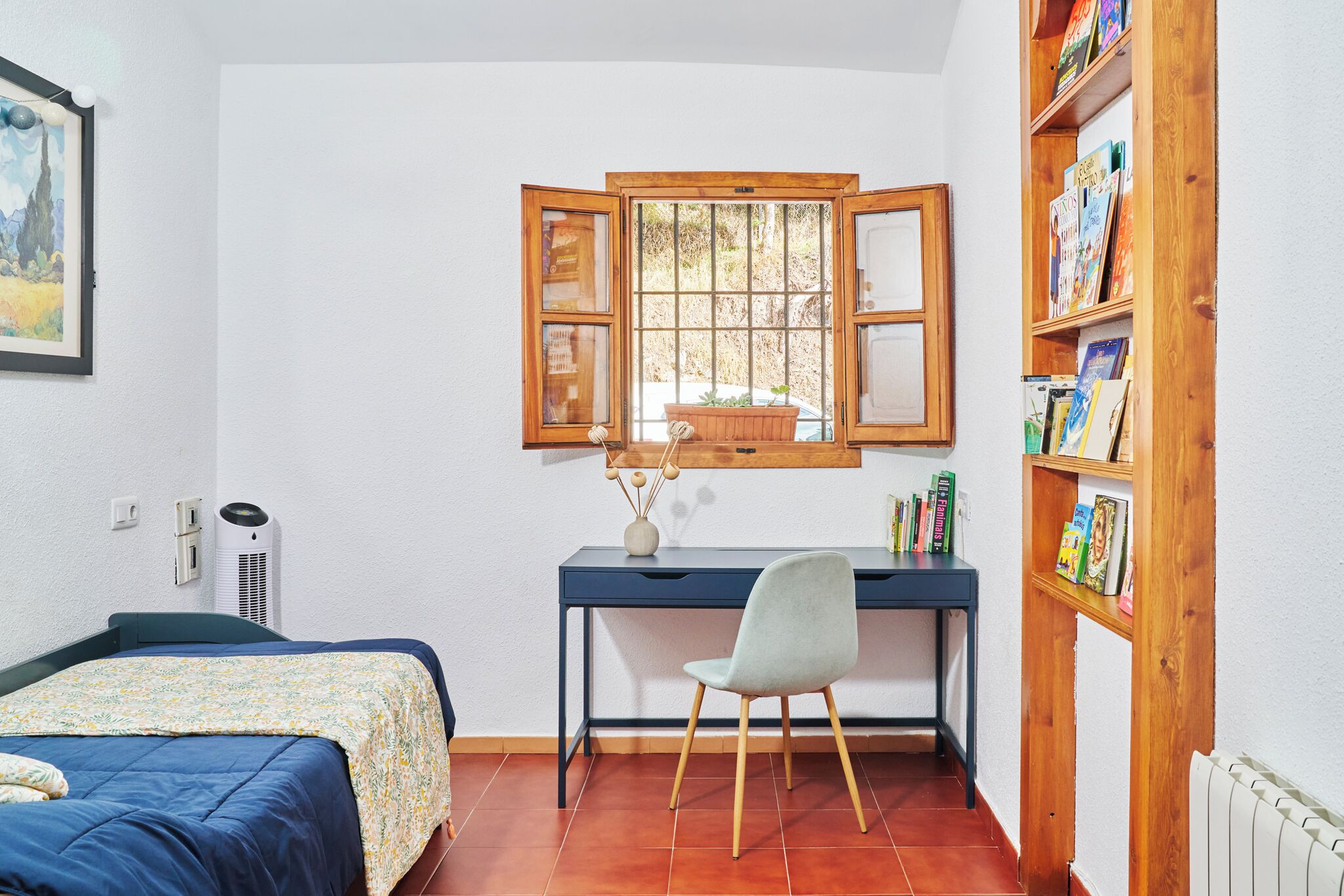 Un dormitorio con una cama, un escritorio con silla, una ventana y una estantería.