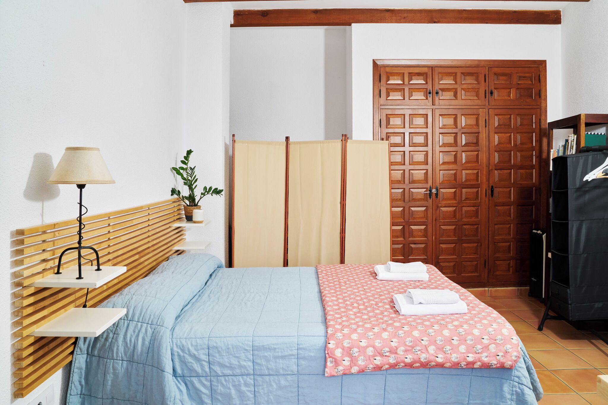 Un dormitorio con cama, mesita de noche, lámpara, planta, armario y closet.