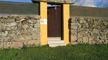 Una entrada de pared de piedra con una puerta de madera, una pequeña estructura de piedra encima de la puerta y un área cubierta de césped al frente.