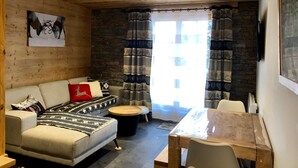 A cozy living room with a sofa, a round wooden coffee table, and a dining table with chairs. - BEAUTIFUL T3 ESPRIT CHALET (LES ANGLES)